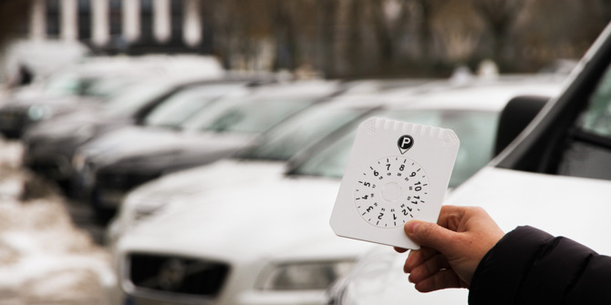 Hand som håller p-skiva framför en rad med parkerade bilar