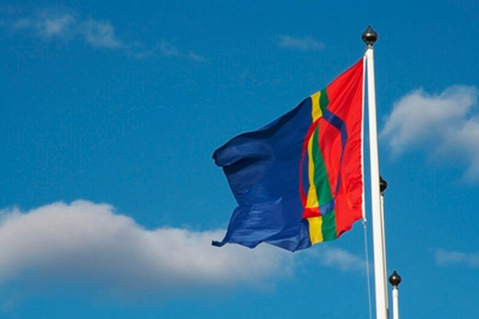 samisk flagga hissad i flaggstång mot blå himmel